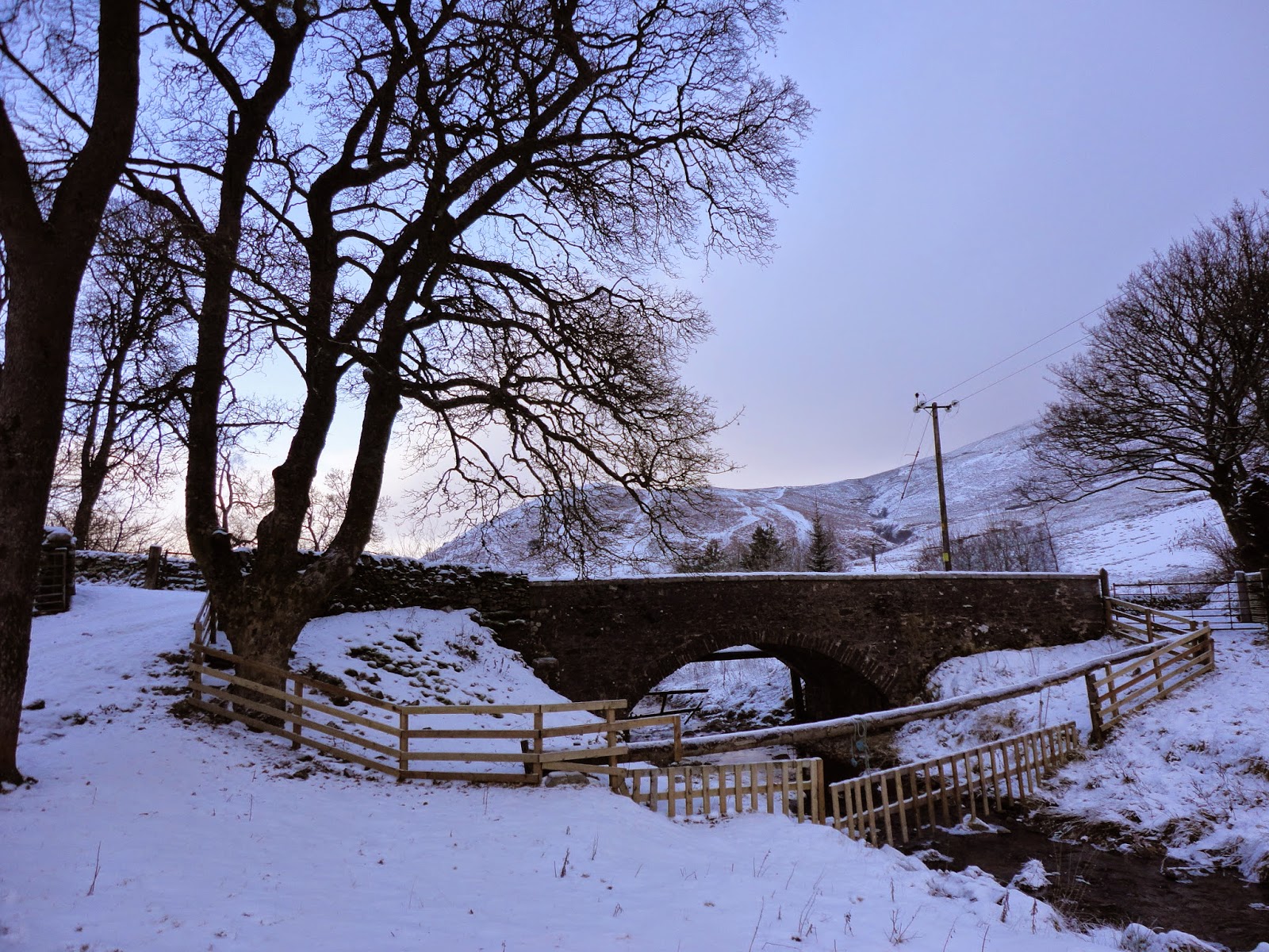 country farm landscape with trees, hills, river, bridge and snow in winter in scotland
