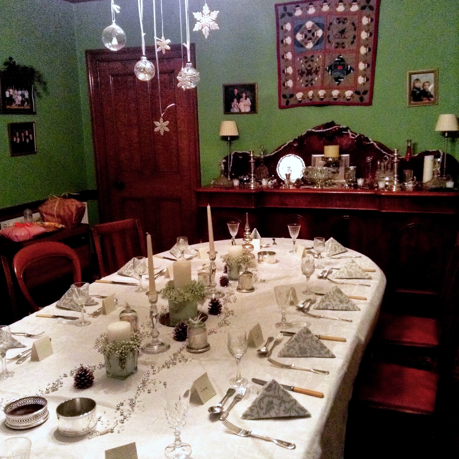 Christmas dinner table with white & silver napkins, candles, pine cones & dangling ornaments on light fixture