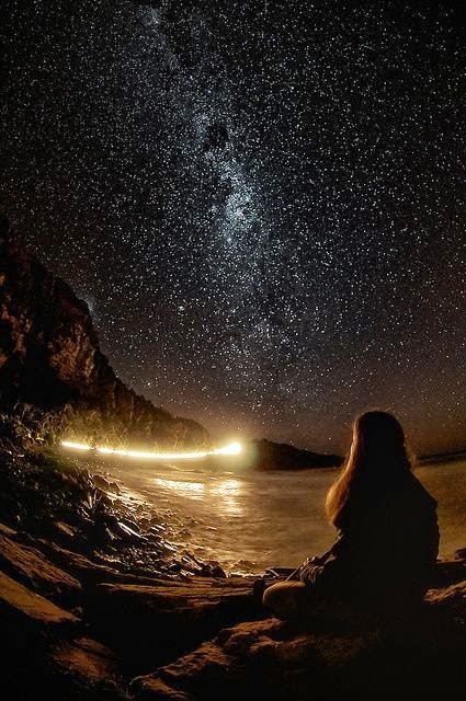 Girl sitting by the ocean at night, looking up to the stars and the universe