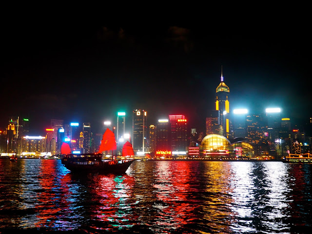 A Symphony of Lights | view of Hong Kong island and Victoria Harbour from TST promenade at night with traditional Chinese junk boat