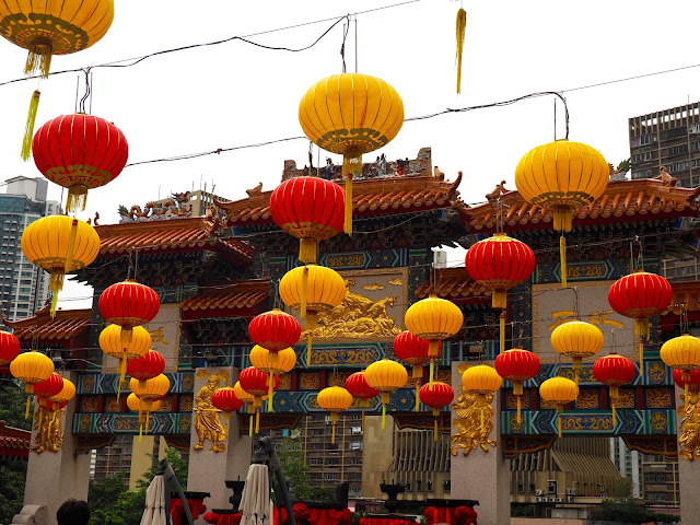 Red & yellow Chinese lanterns hanging in the courtyard of Sik Sik Yuen Wong Tai Sin Temple, with the ornamental archway in the background | Hong Kong