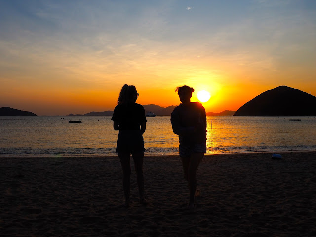 Silhouettes of two girls on the beach, against the sunset over the ocean on Repulse Bay Beach, Hong Kong