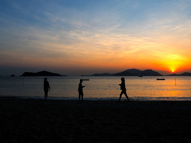 Silhouettes of three girls on the sand against the sunset over the ocean on Repulse Bay Beach, Hong Kong
