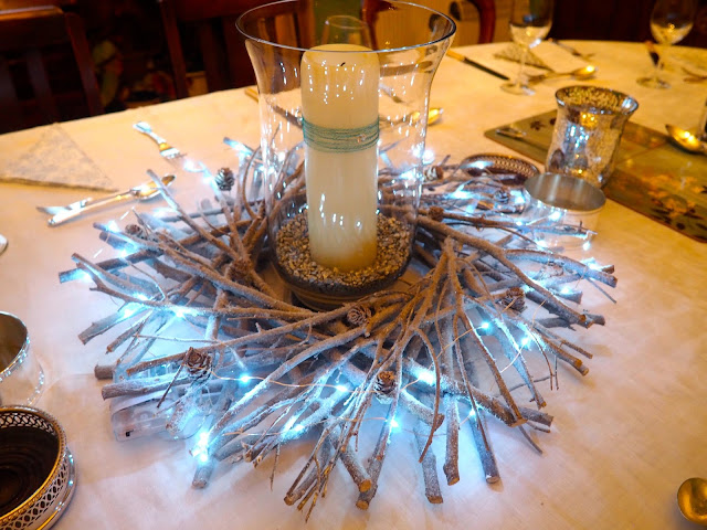 Centrepiece for the Christmas dinner table, a wooden stick wreath with blue lights, and a glass vase with a big white candle