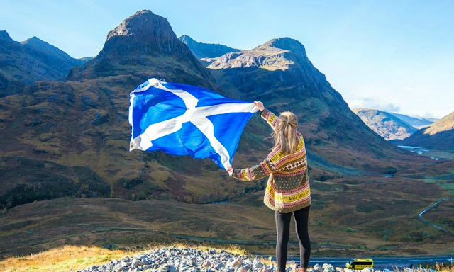 Girl holding Scottish saltire flag in front of Highlands mountains