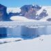 Antarctica Expedition part 1 - feature photo - pair of Gentoo penguins in the snow with icy water next to them and snowy mountains in the background - Croft Bay on James Ross Island