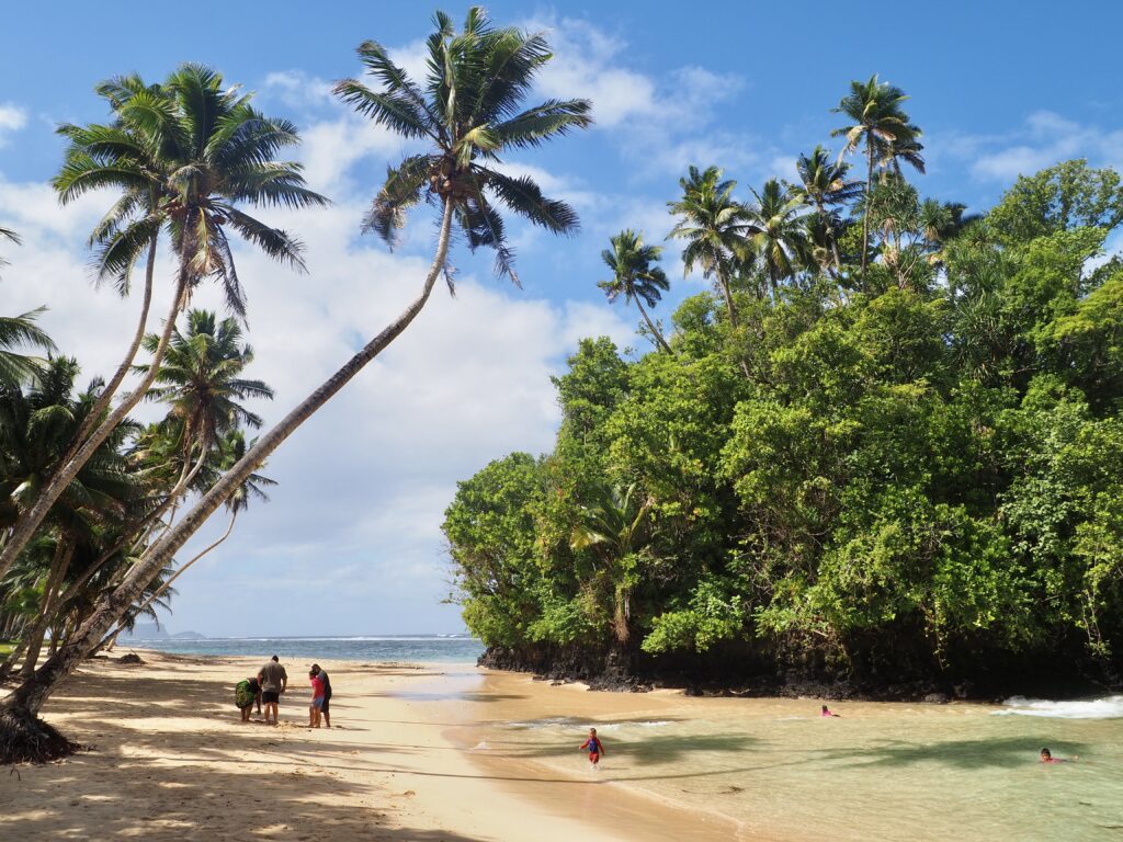 A Week in Samoa - feature photo - palm trees over white sand Vavau beach and a small tree-covered peninsula