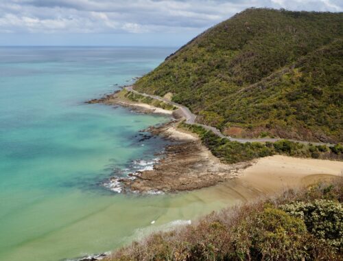 Great Ocean Road trip - feature photo - road curving around the coast, between a hill and blue ocean - view from Teddy's Lookout, Lorne, Victoria, Australia