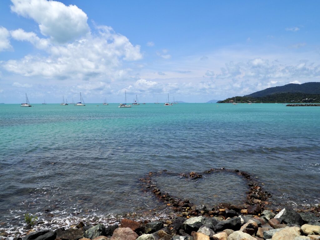 Weekend in the Whitsundays - second feature photo - heart made of pebbles in the shallows off the coast, with sailing boats on the horizon at Airlie Beach, Queensland, Australia