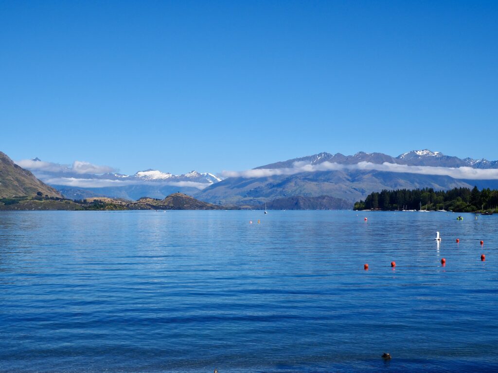 A Week in Wānaka - second feature photo - blue water of Lake Wānaka under blue sky, with snow-capped mountains and a thin line of cloud in the background - New Zealand, South Island